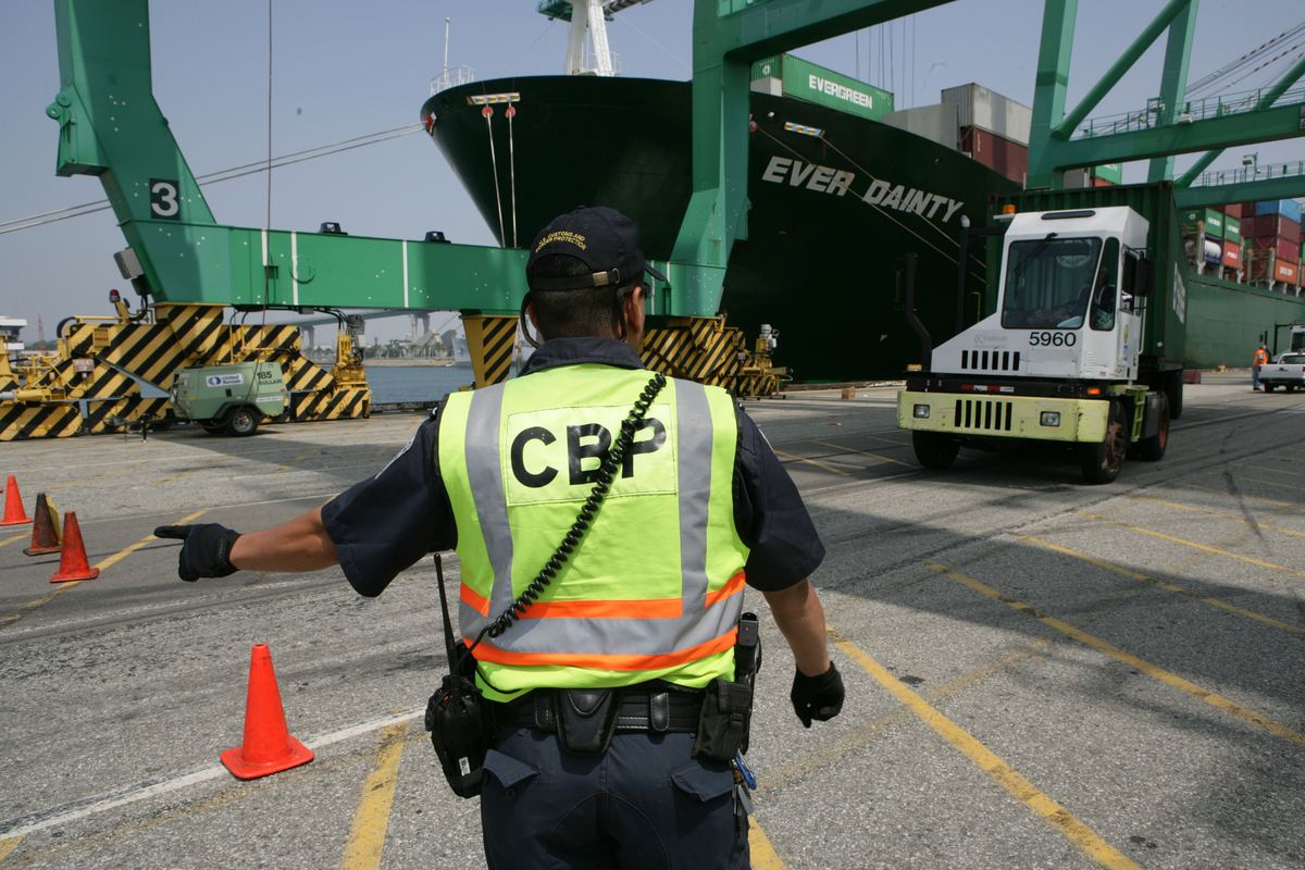 A U.S. Customs and Border Protection officer directs a truck carrying a seaport container toward an inspection area at the Port of Los Angeles.